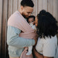 Family with a baby in Mushie Baby Wrap, standing close together outdoors.