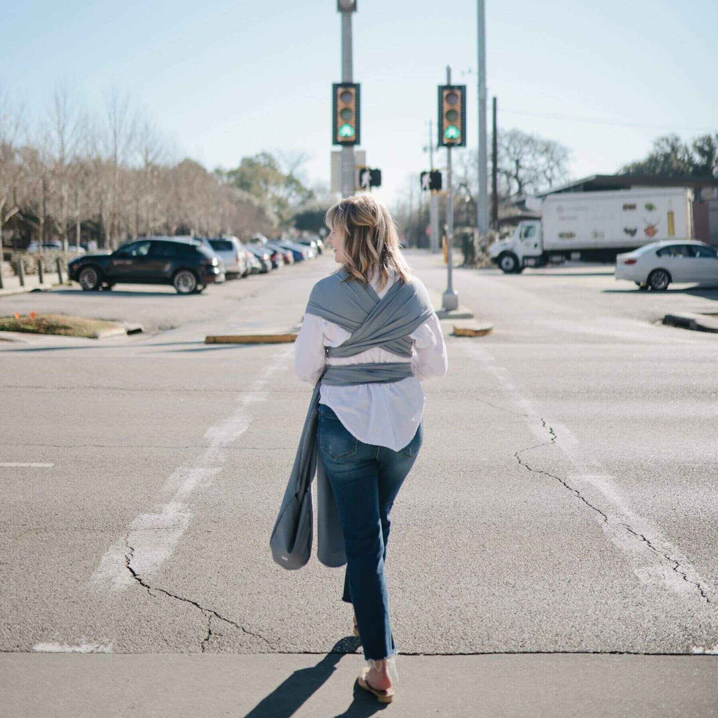 Woman walking on a street with a baby in Mushie Baby Wrap