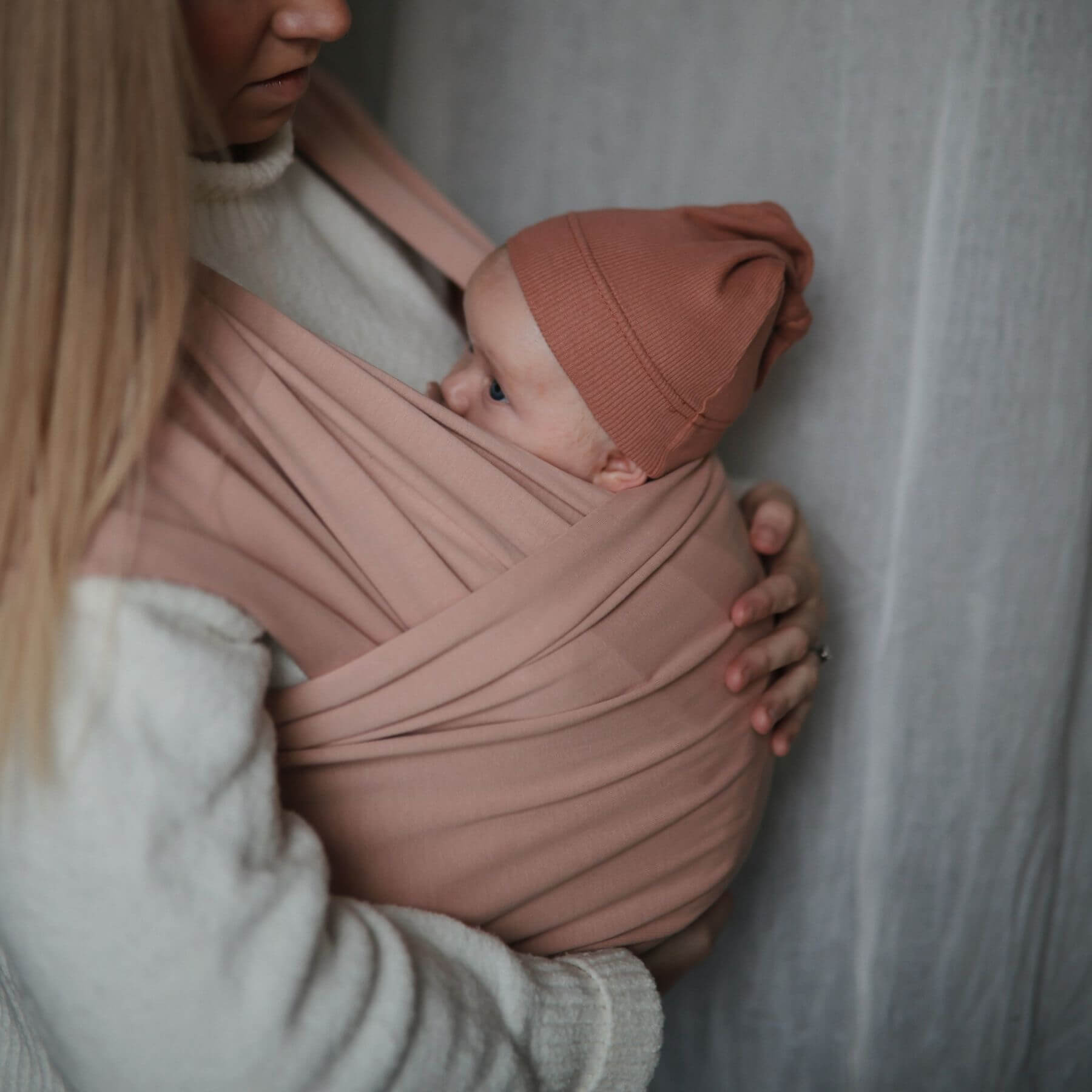 Person holding a baby wrapped in Mushie Baby Wrap against a neutral background