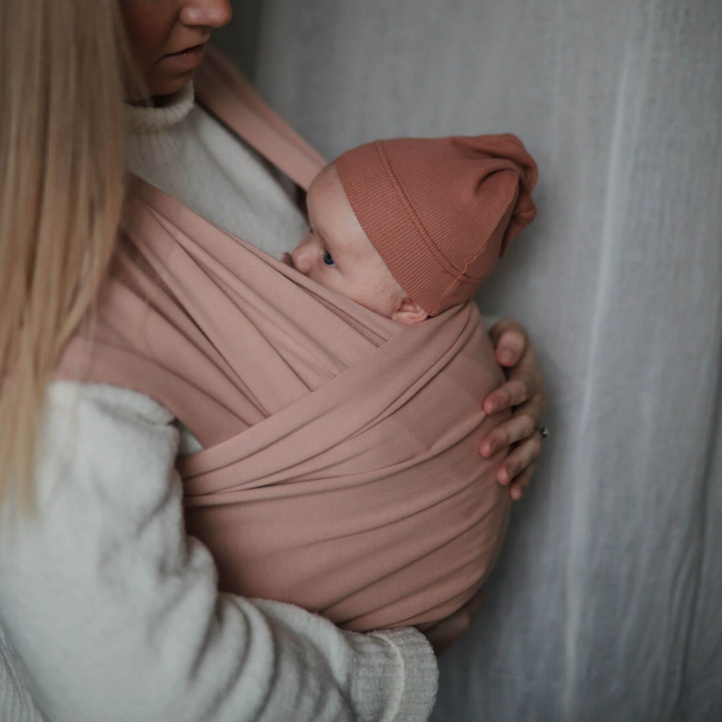 Person holding a baby wrapped in Mushie Baby Wrap against a neutral background