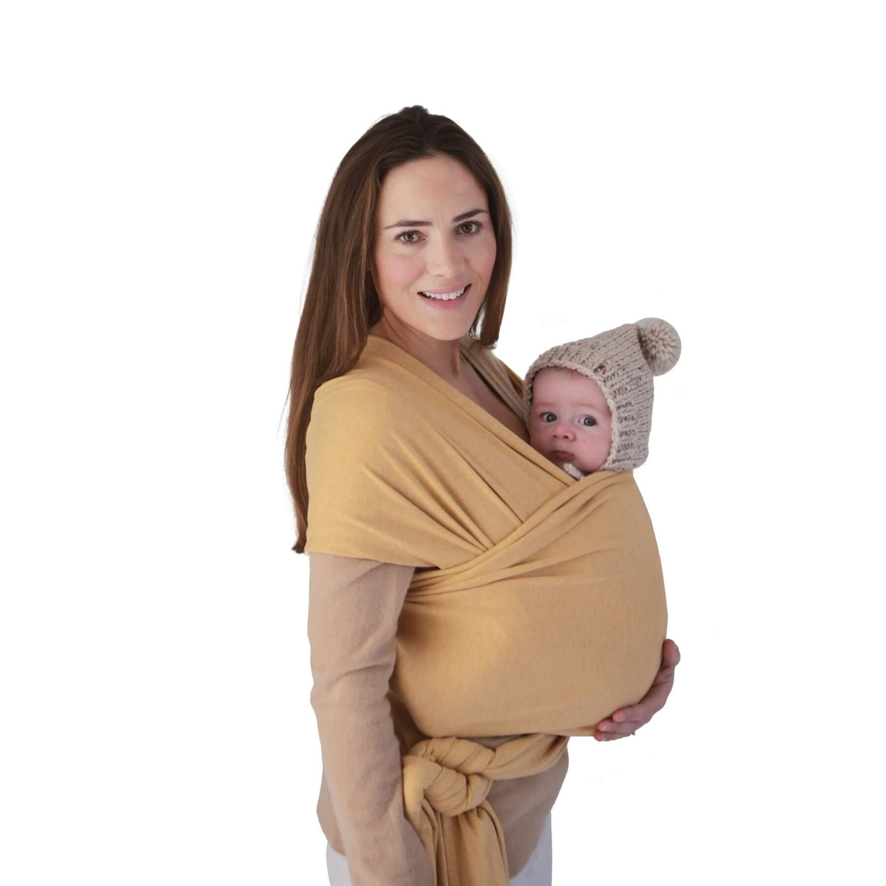 Woman holding a baby in Mushie Baby Wrap Mustard melange against a white background