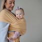 Woman holding a baby wrapped in Mushie Baby Wrap against a plain background