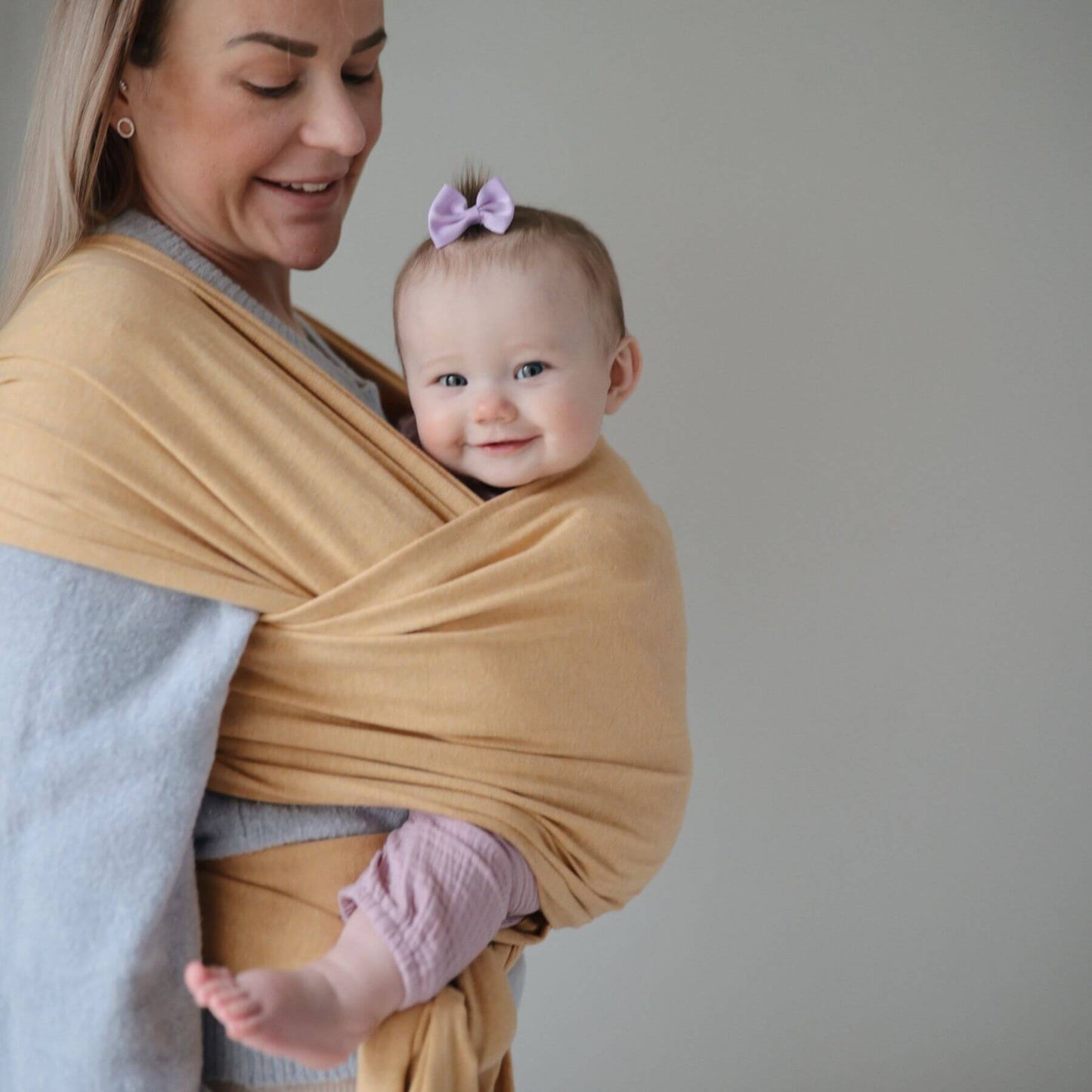 Woman holding a baby wrapped in Mushie Baby Wrap against a plain background