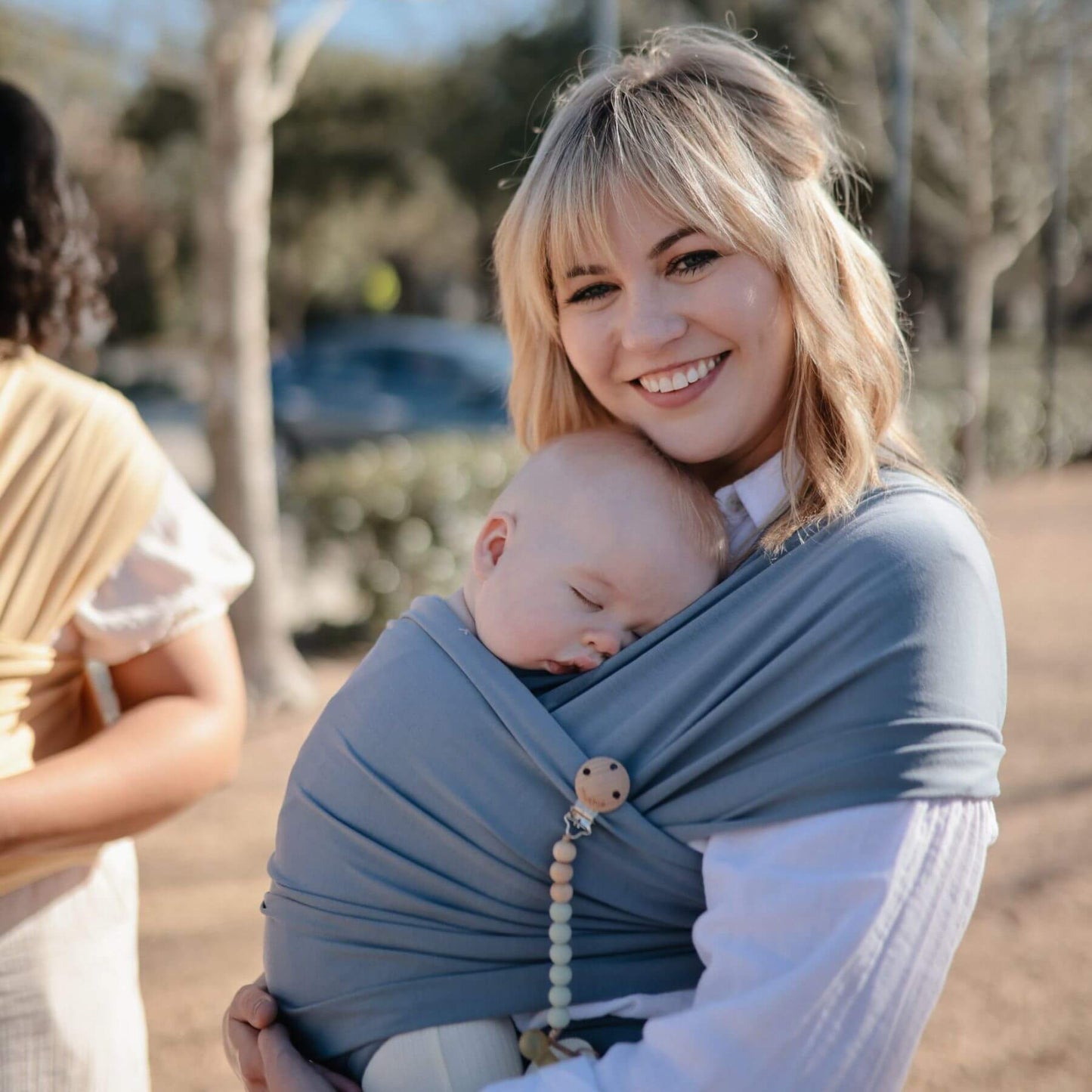 Woman holding a baby in a Mushie Baby Wrap outdoors