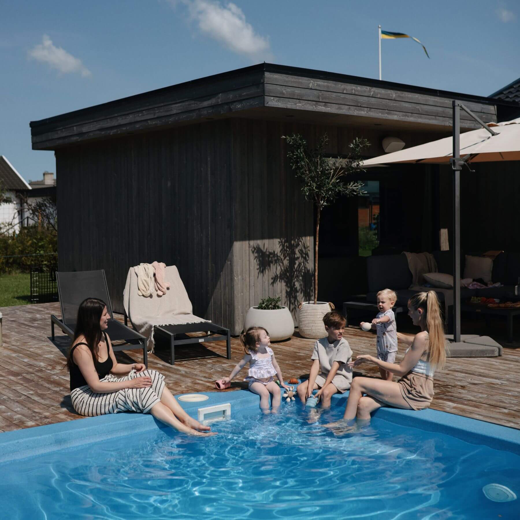 People by a pool with a wooden deck and outdoor furniture