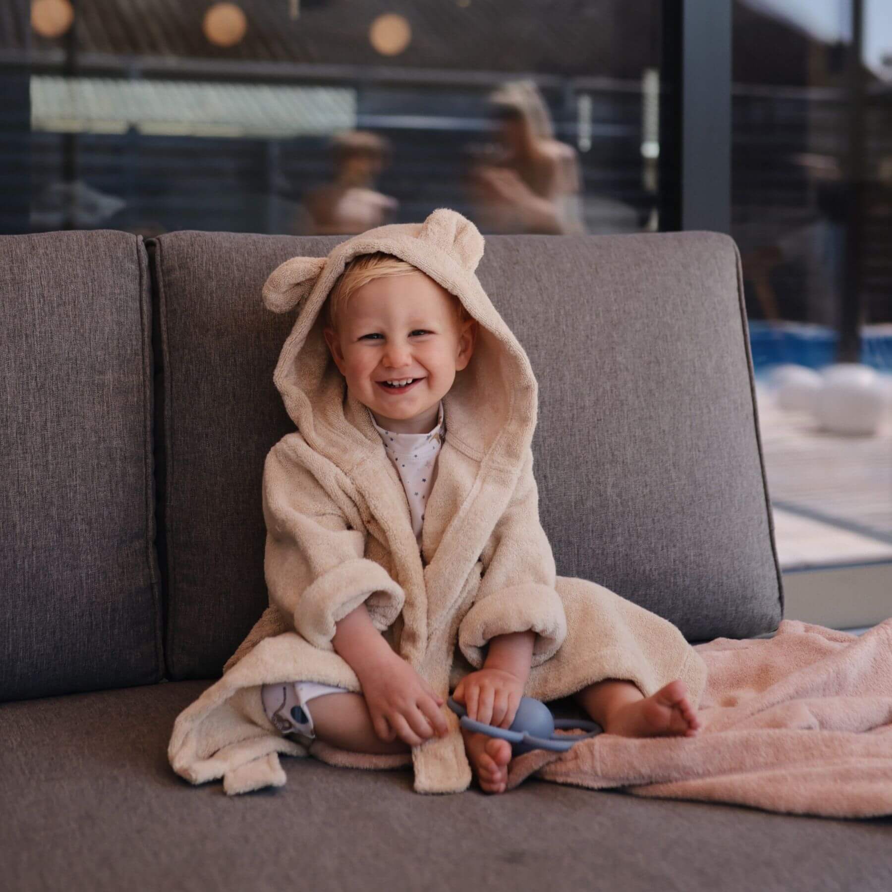 Child in Mushie Bear Robe sitting on a couch indoors.