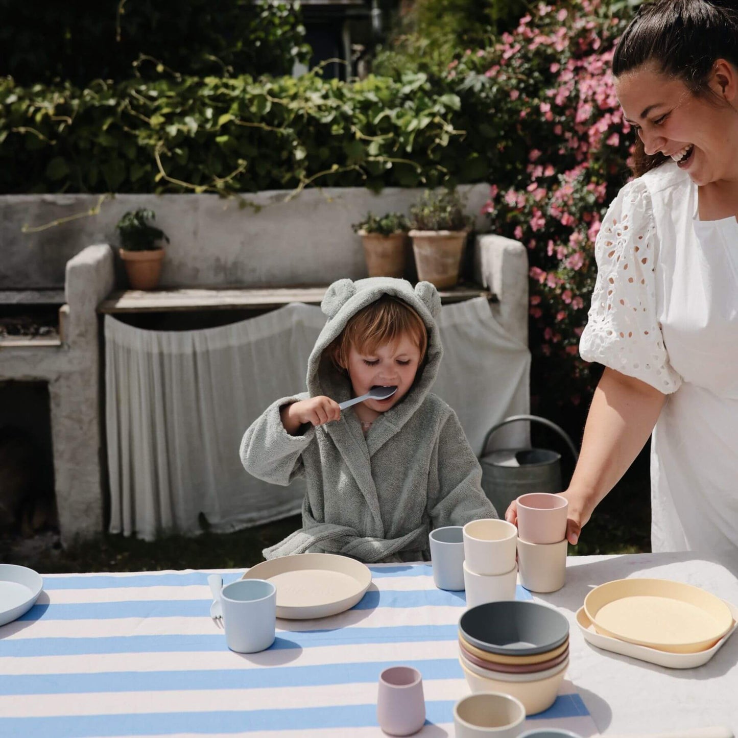 Woman and child in Mushie Bear Robe at a table with ceramic items outdoors