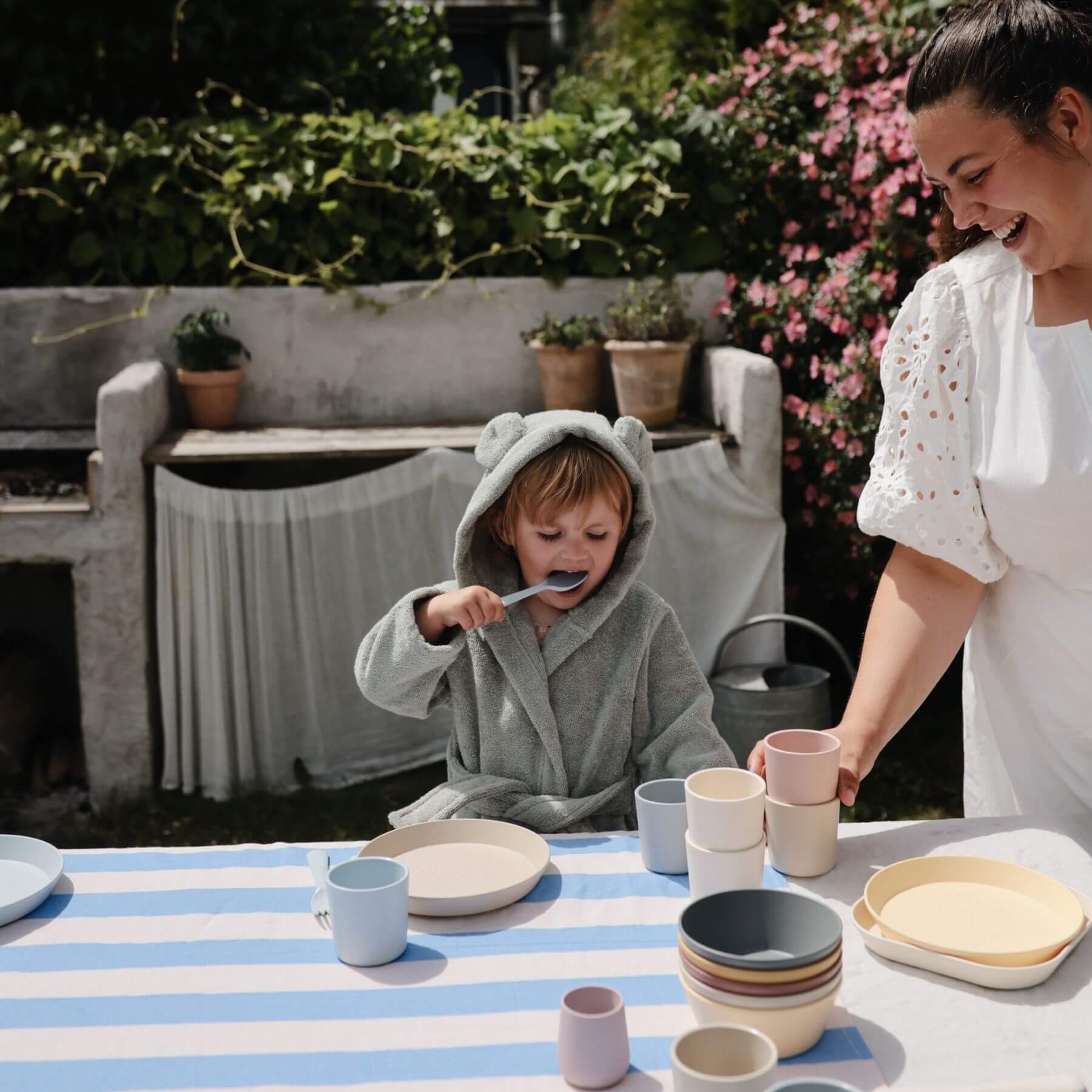 Woman and child in Mushie Bear Robe at a table with ceramic items outdoors