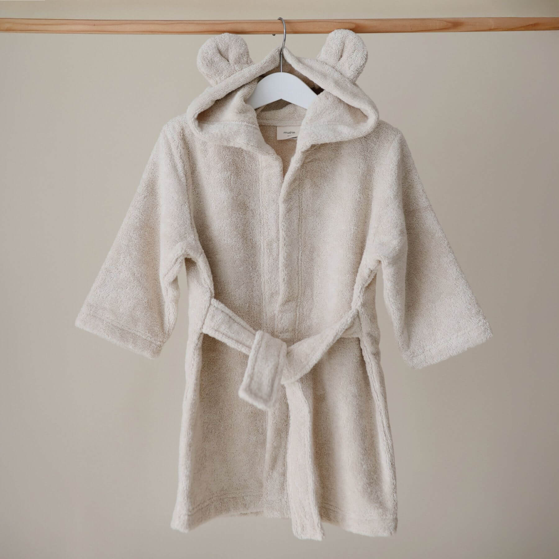 Mushie Bear Robe Beige on a hanger against a beige wall