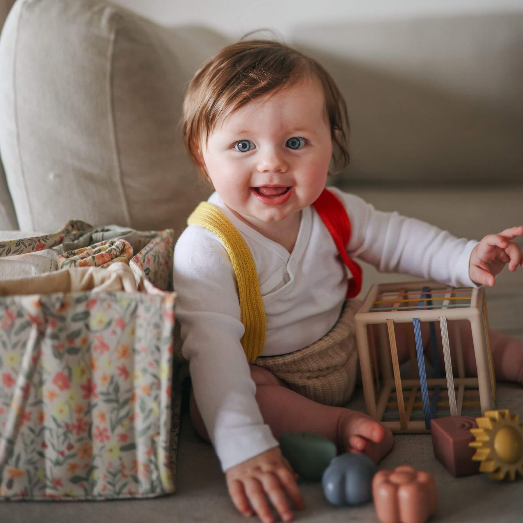 Baby sitting on sofa with toys and a Mushie Diaper Caddy