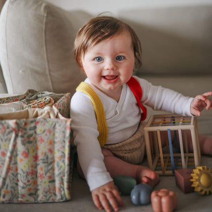 Baby sitting on sofa with toys and a Mushie Diaper Caddy