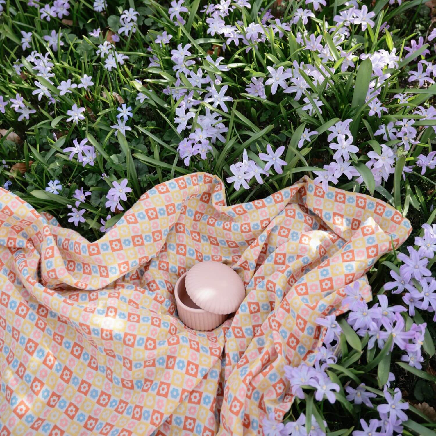 Colorful patterned blanket on grass with small flowers