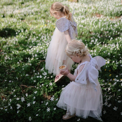 Two young girls in white dresses standing in a field of small white flowers.