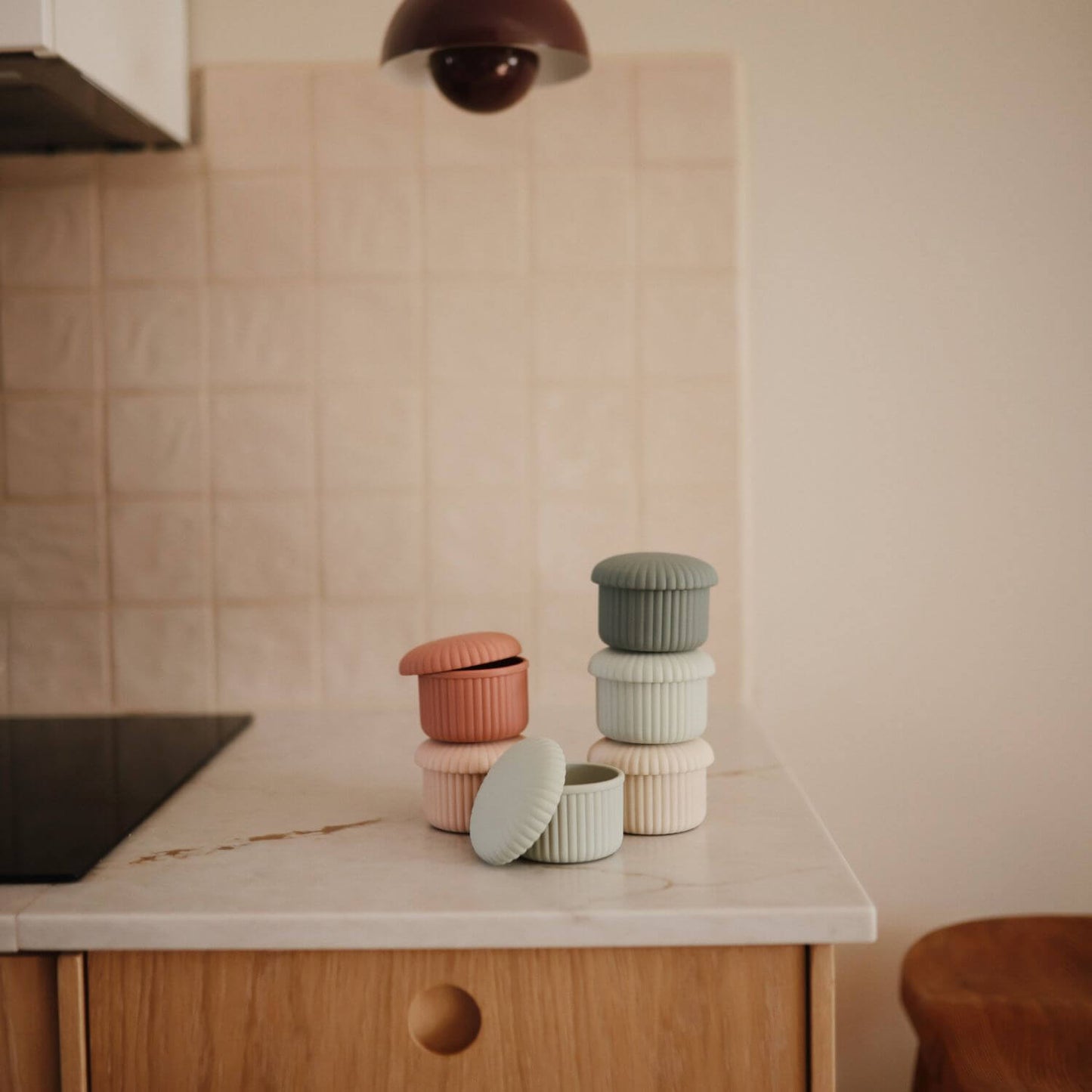 Mushie Silicone Baby Food Containers in muted pastel colors arranged on a kitchen countertop