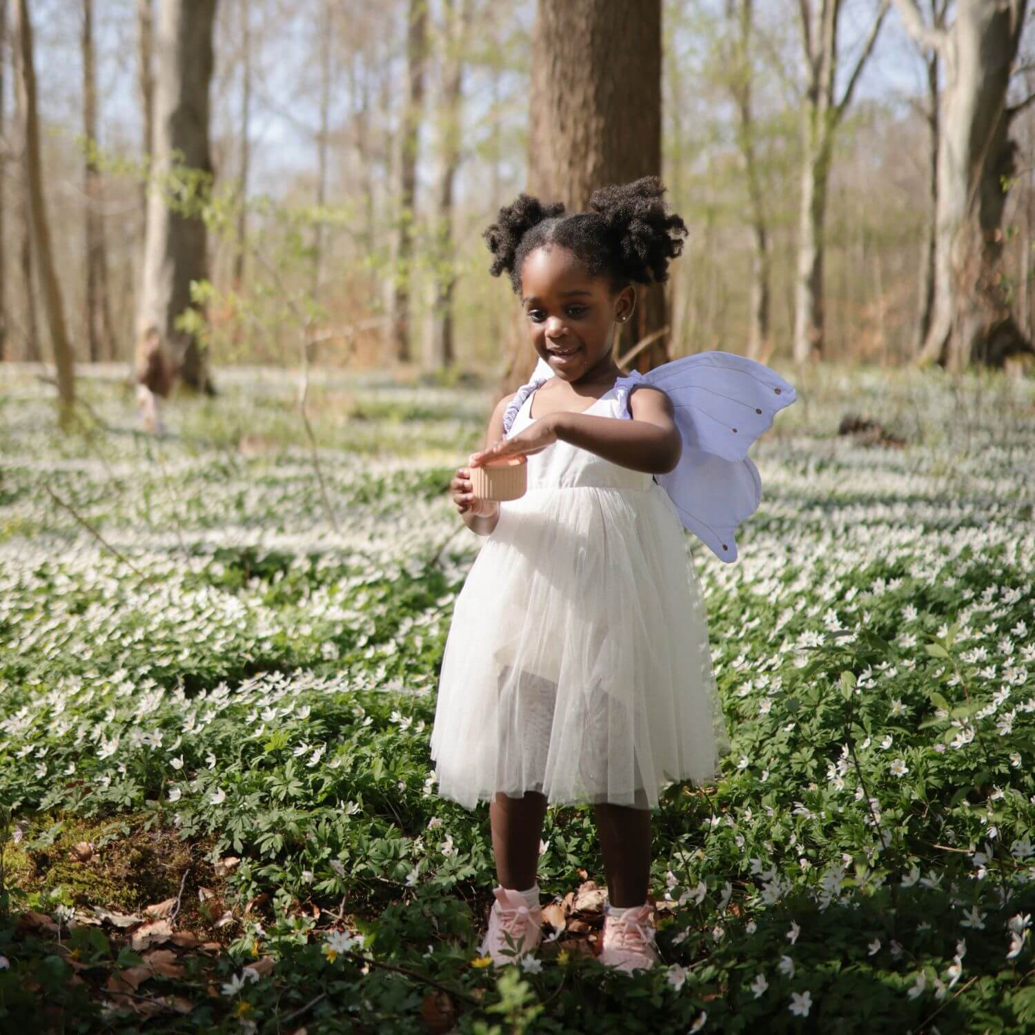 Young girl in a white dress with fairy wings standing in a field of white flowers.