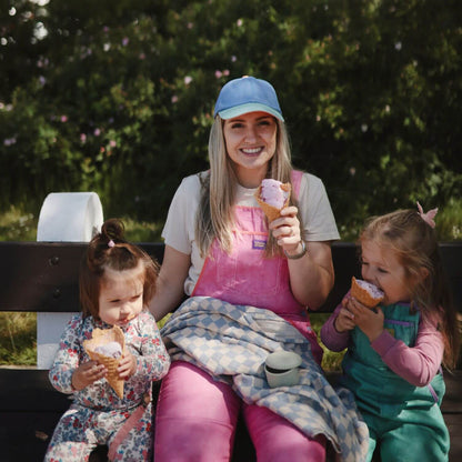 Woman with two children sitting on a bench eating ice cream in a park.
