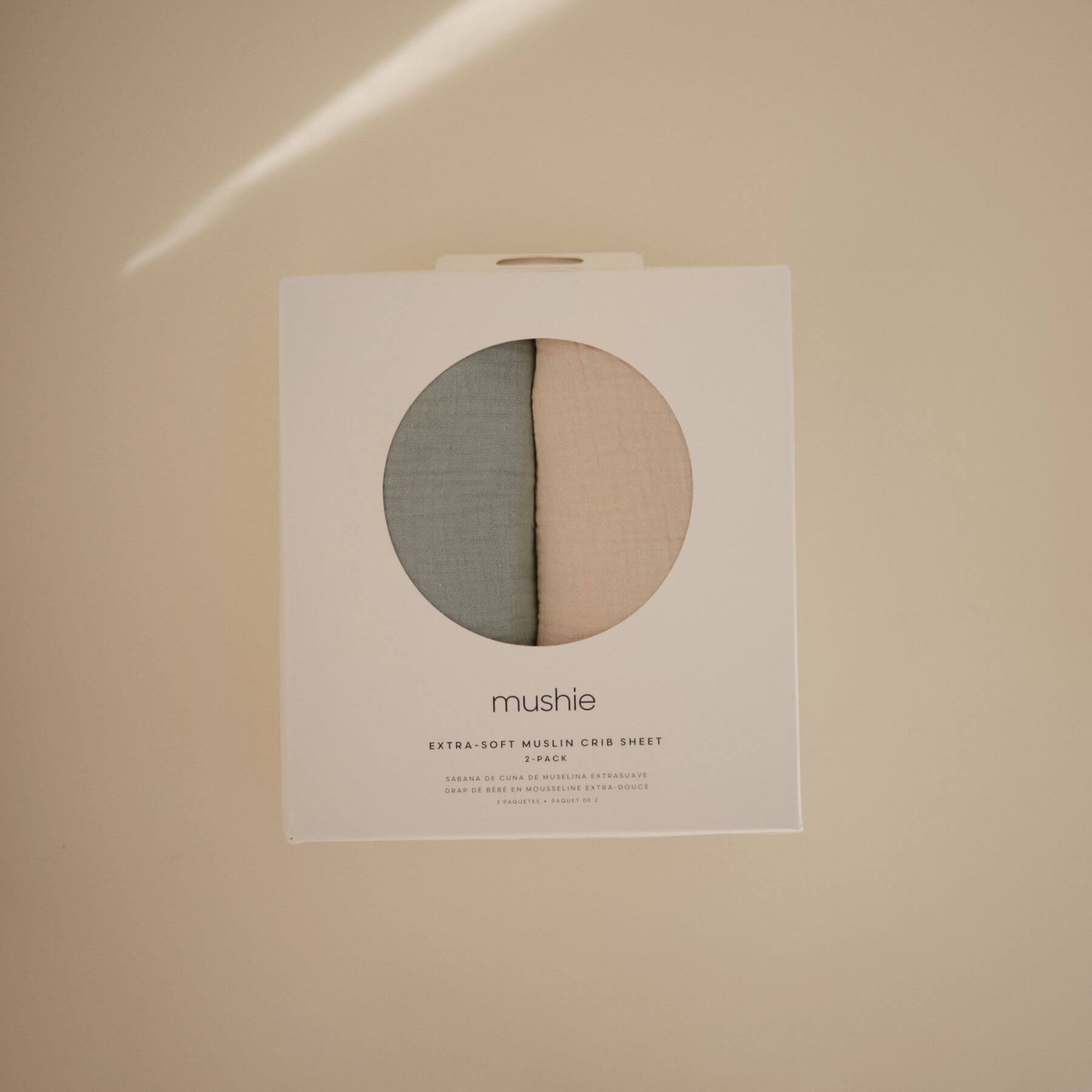 Mushie crib sheet packaging on a beige background