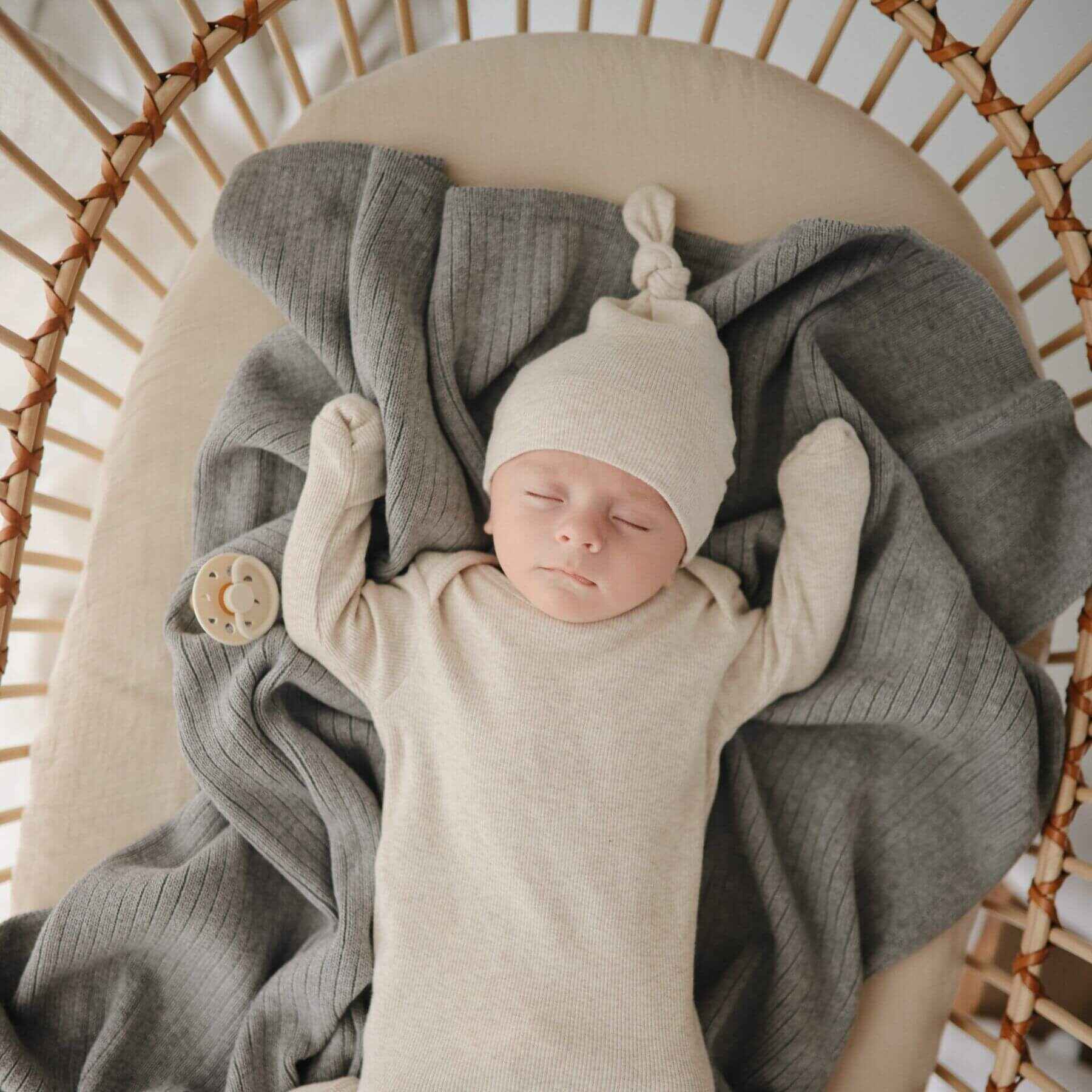 Newborn baby sleeping in a wicker basket with gray and beige blankets