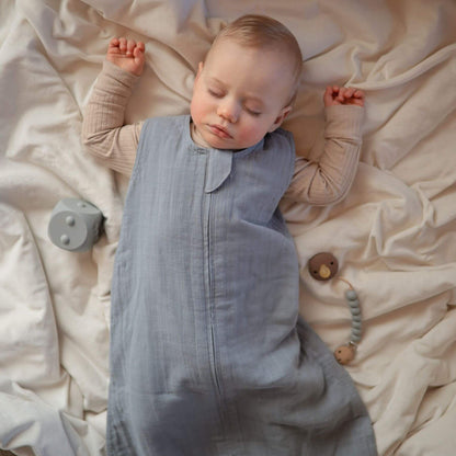Baby sleeping in Mushie Organic Cotton Sleep Bag on a soft beige blanket with toys around