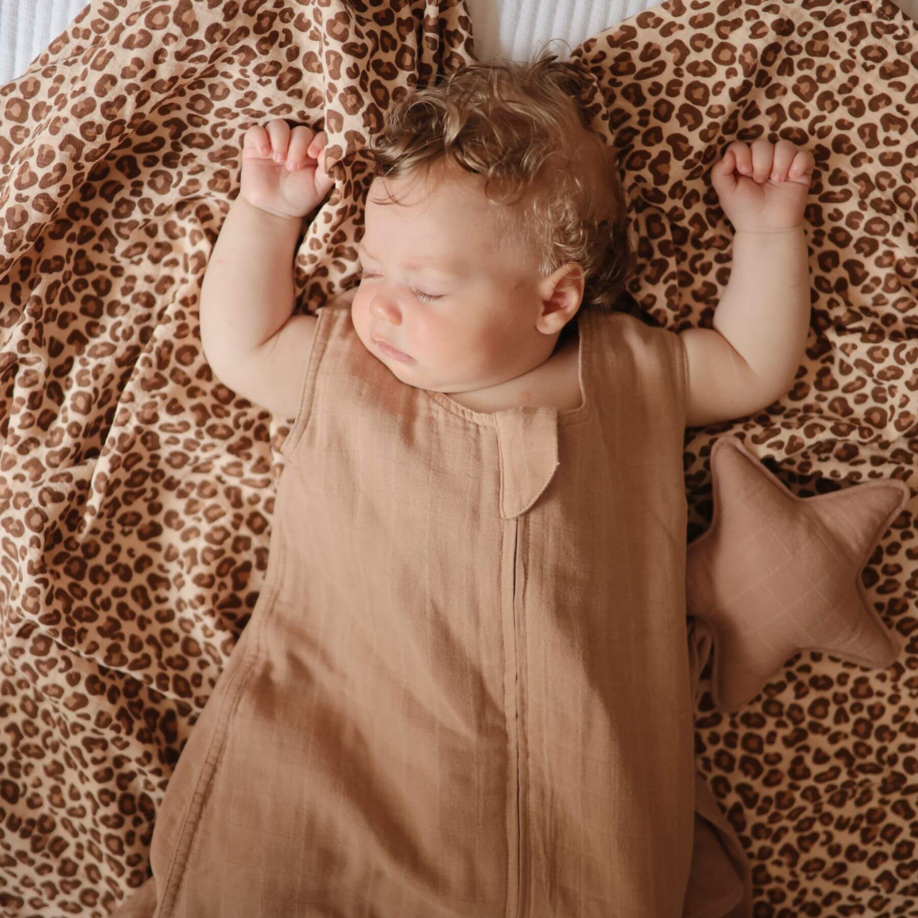 Baby lying on a leopard print blanket wearing Mushie Organic Cotton Sleep Bag