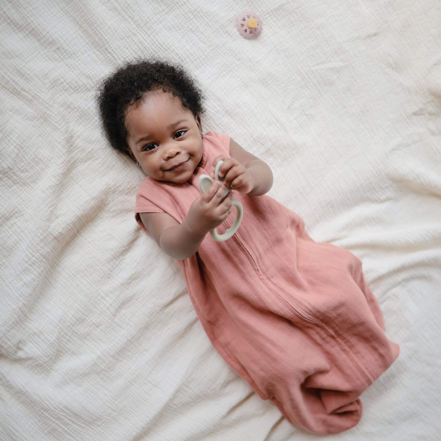 Baby in Mushie Organic Cotton Sleep Bag lying on a white blanket