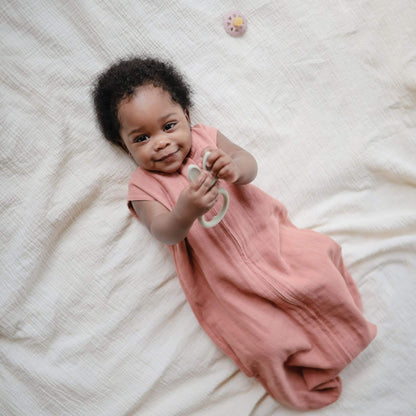 Baby in Mushie Organic Cotton Sleep Bag lying on a white blanket
