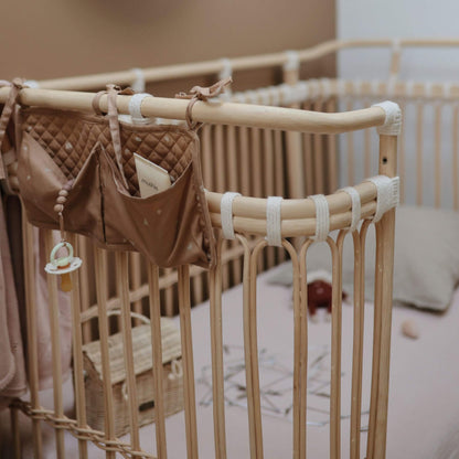 Bamboo crib with baby items including a pacifier and small bag in a nursery setting.