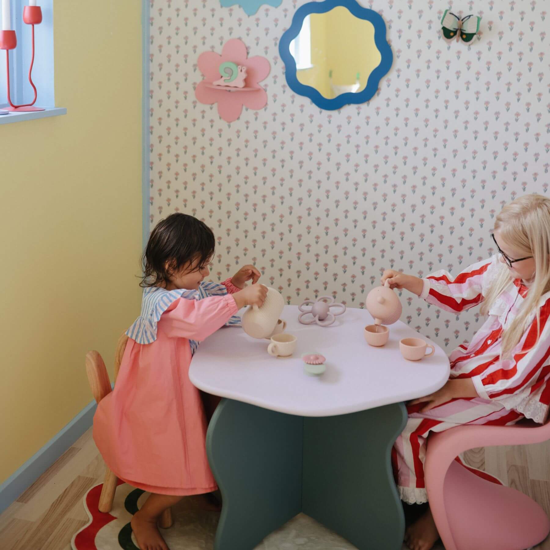Two children playing with Mushie Silicone Tea Play Set at a table in a child-friendly room.