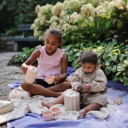 Two young girls sitting on a blanket outdoors with toys.