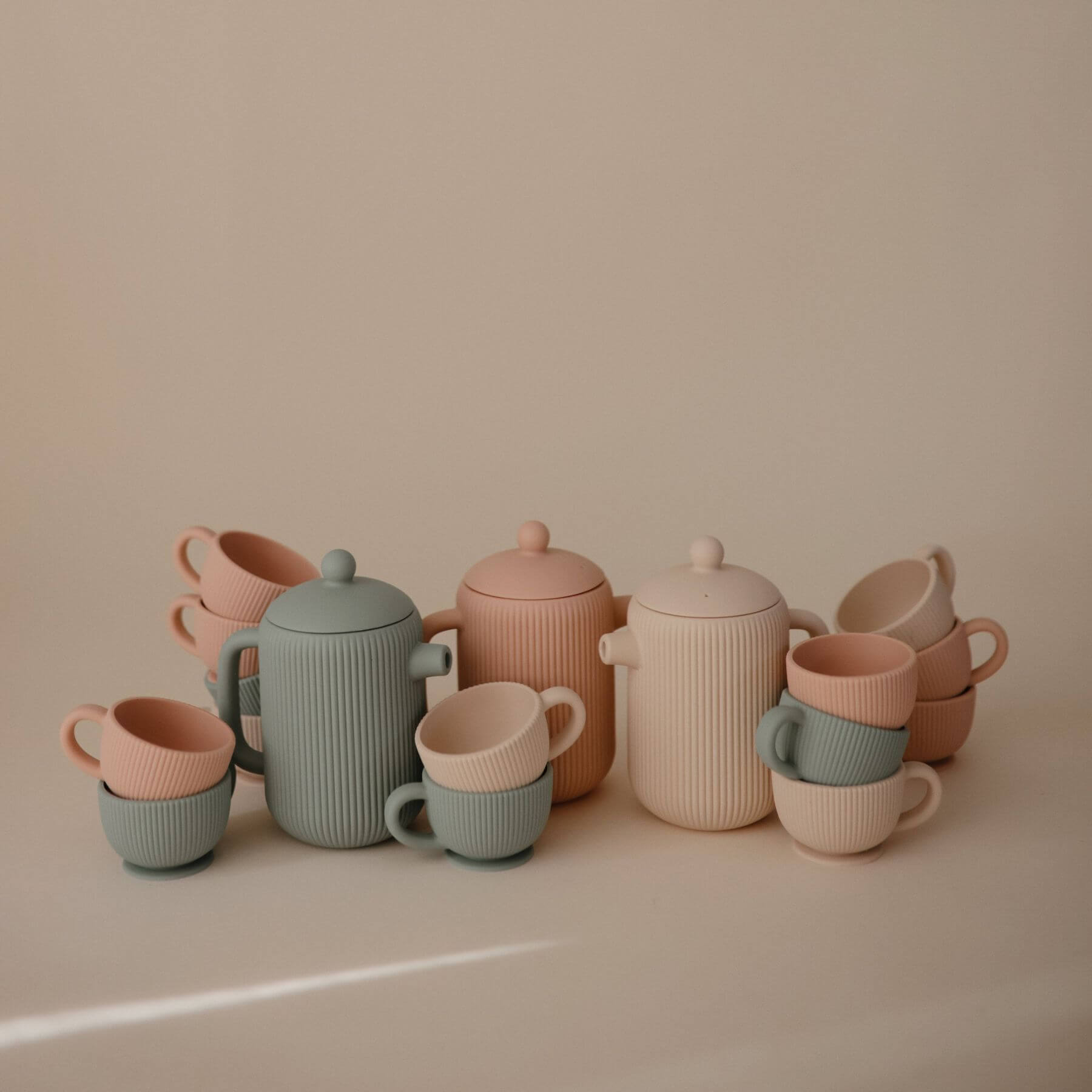 Mushie Silicone Tea Play Sets in pastel colors on a beige background