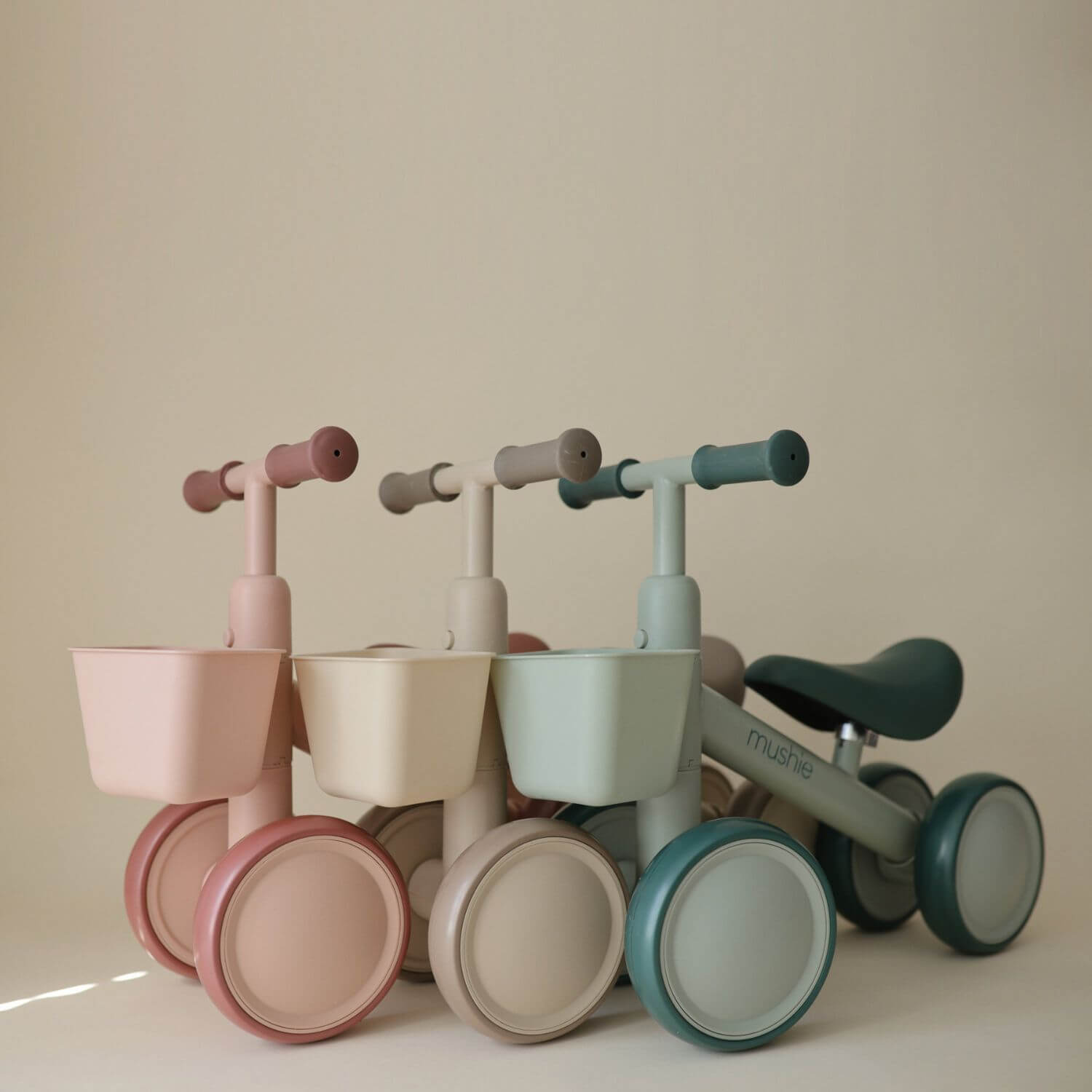 Set of four colorful Mushie Mini Toddler Bikes on a beige background