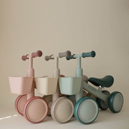 Set of four colorful Mushie Mini Toddler Bikes on a beige background