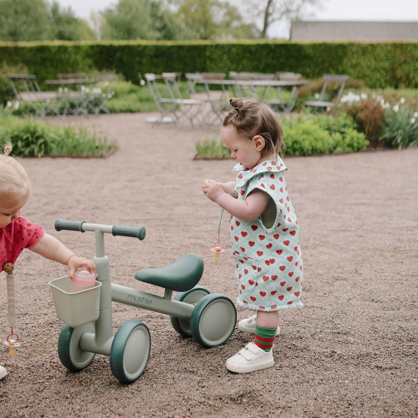 Two children playing with Mushie Mini Toddler Bike in an outdoor setting
