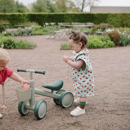 Two children playing with Mushie Mini Toddler Bike in an outdoor setting