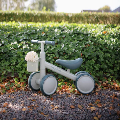 Mushie Mini Toddler Bike sits outdoors on a gravel path in front of a green hedge