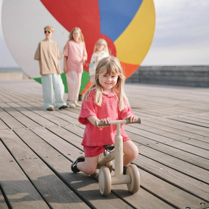 Child on Mushie Mini Toddler Bike with family in the background at a beach.