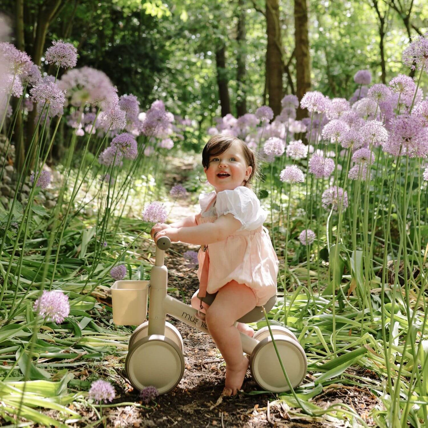 Child on Mushie Mini Toddler Bike in a garden with purple flowers