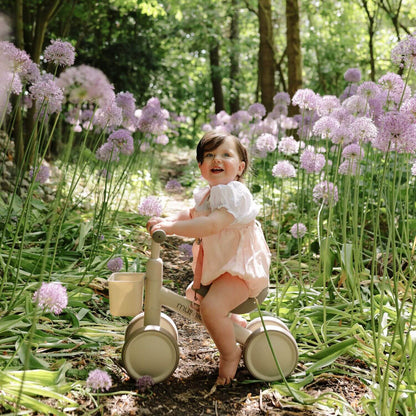 Child on Mushie Mini Toddler Bike in a garden with purple flowers