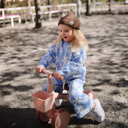 Child riding Mushie Mini Toddler Bike outdoors on a sandy or gravelly surface.