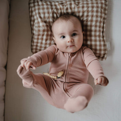 Baby in Mushie Zipper Pajama - Blush lying on a checkered cushion