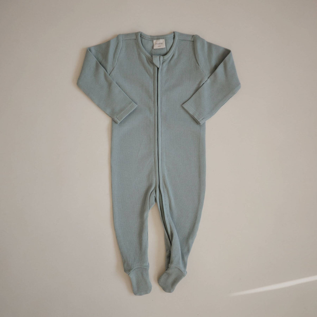 Mushie Zipper Pajama - Green, laid flat on a light beige background.
