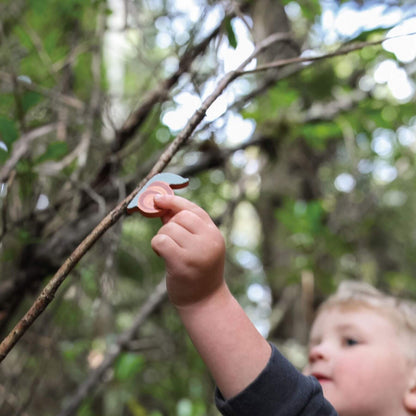 Child holding a snail toy up to a tree branch in a forest setting