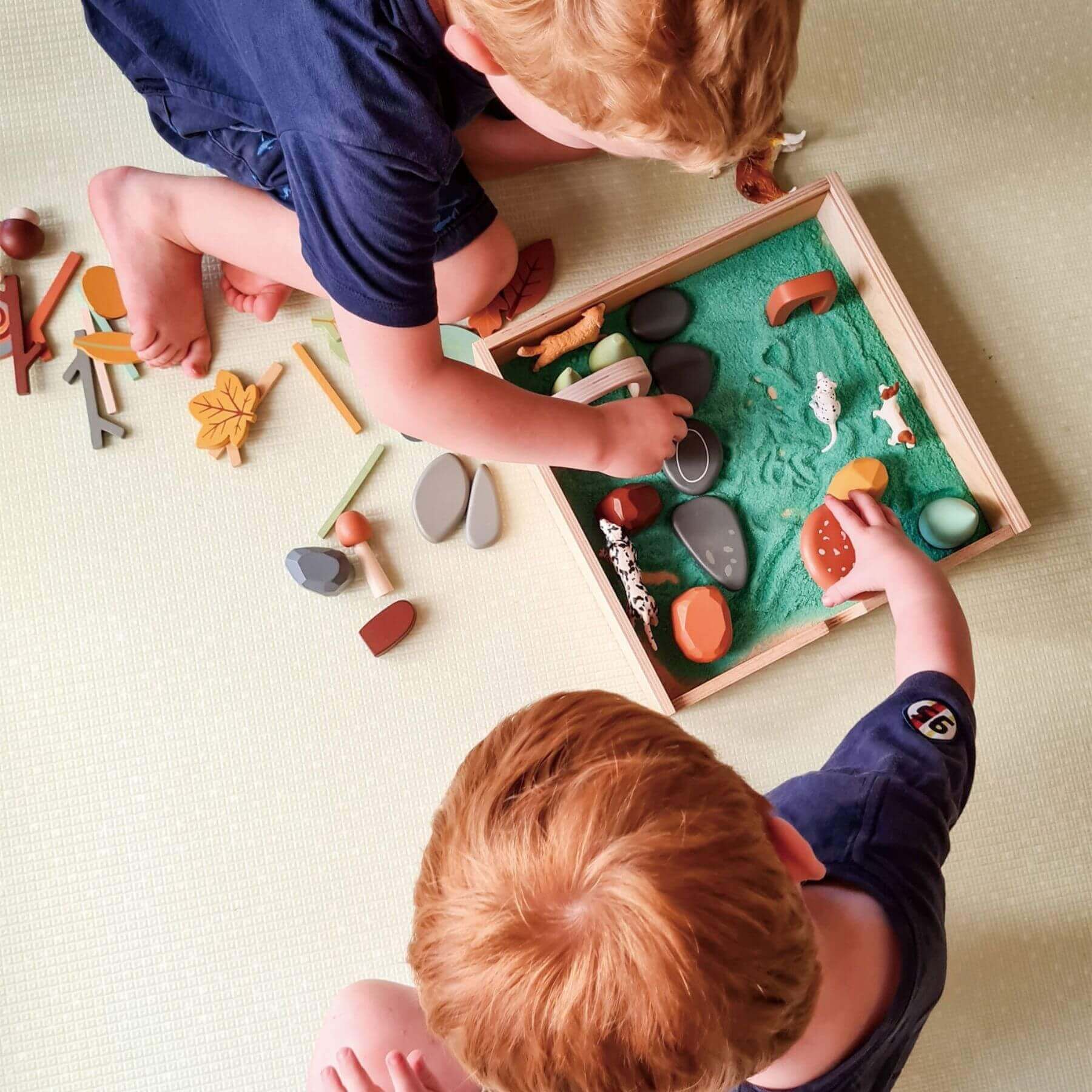 Two children playing with Tender Leaf My Forest Floor on a beige surface.