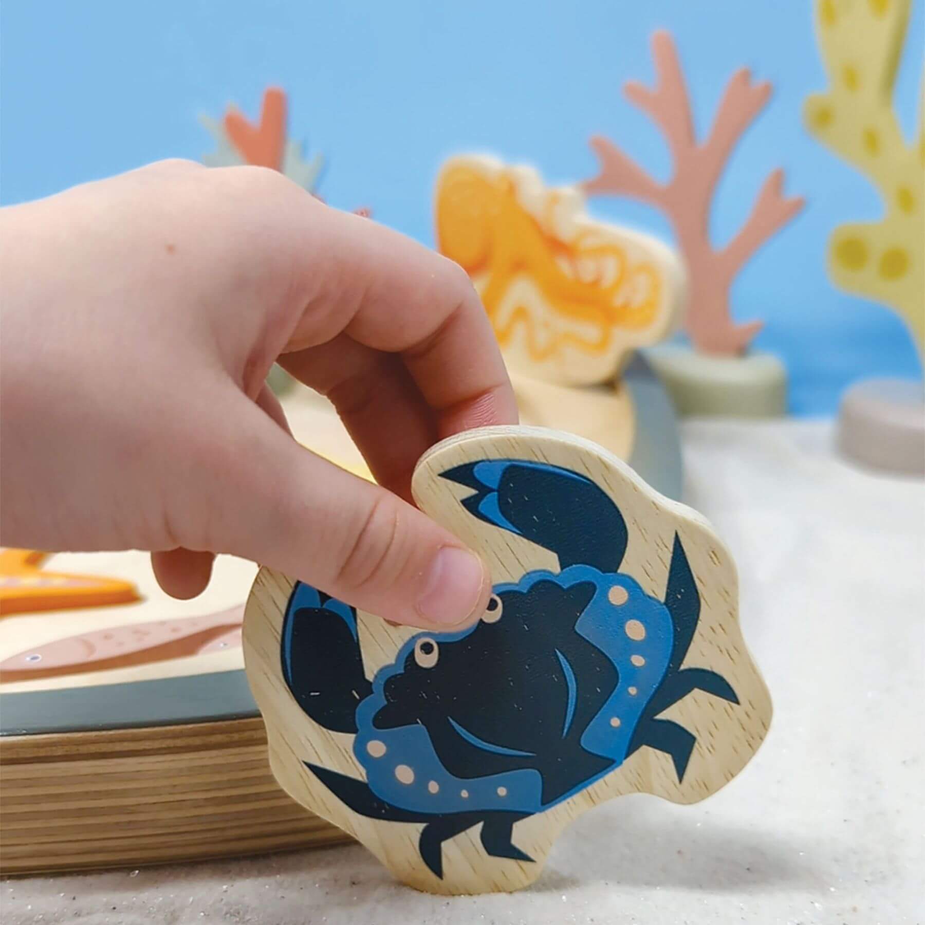 Hand holding a wooden crab toy with a colorful underwater scene in the background