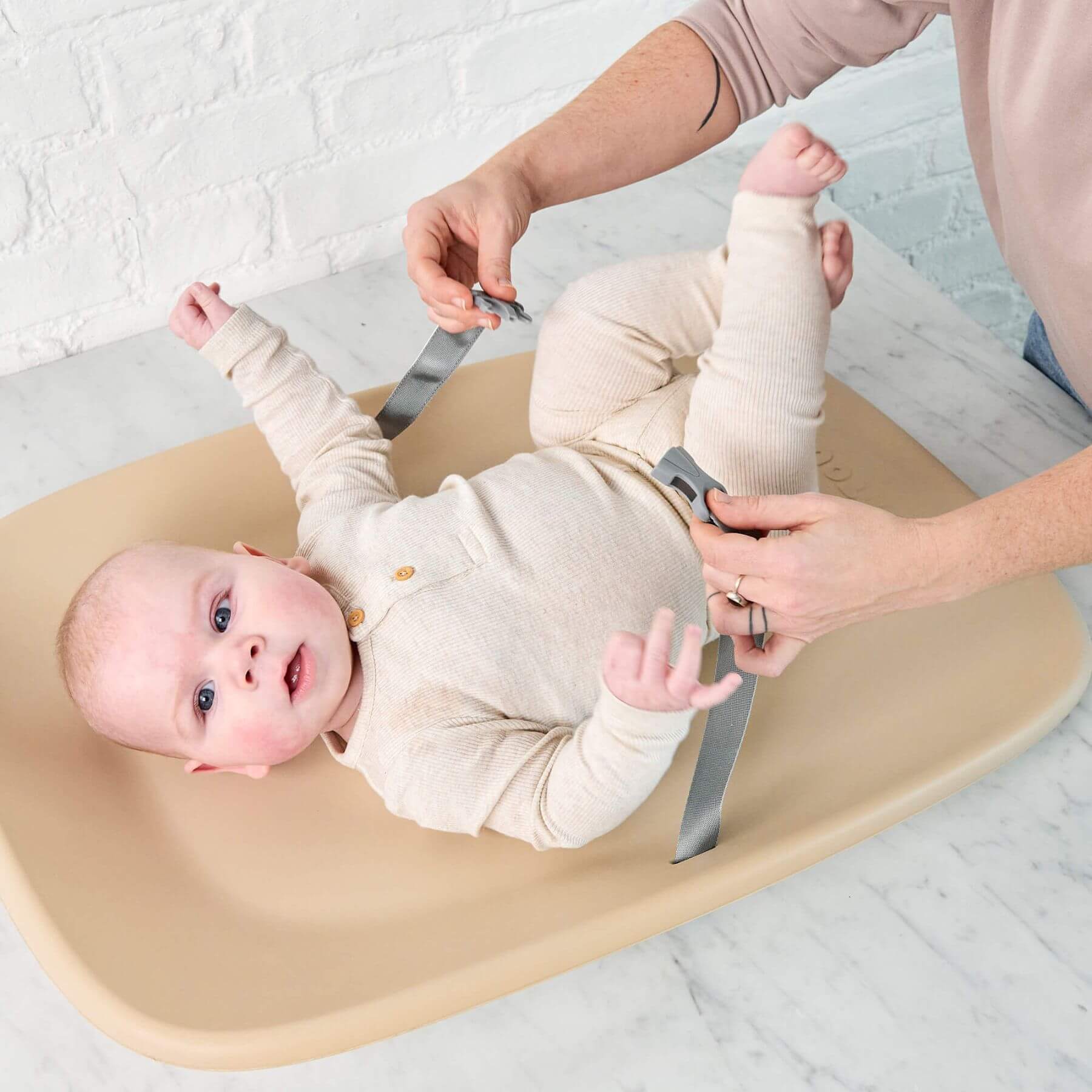 Baby lying on Nattou Diaper Changing Pad Softy Beige with adult hands adjusting straps