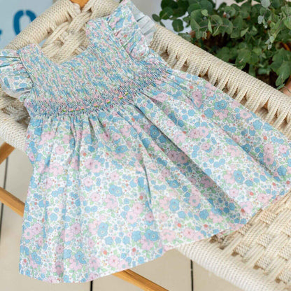 NELIA | Girls Blue Floral Cotton Smocked Dress on a chair with a plant in the background