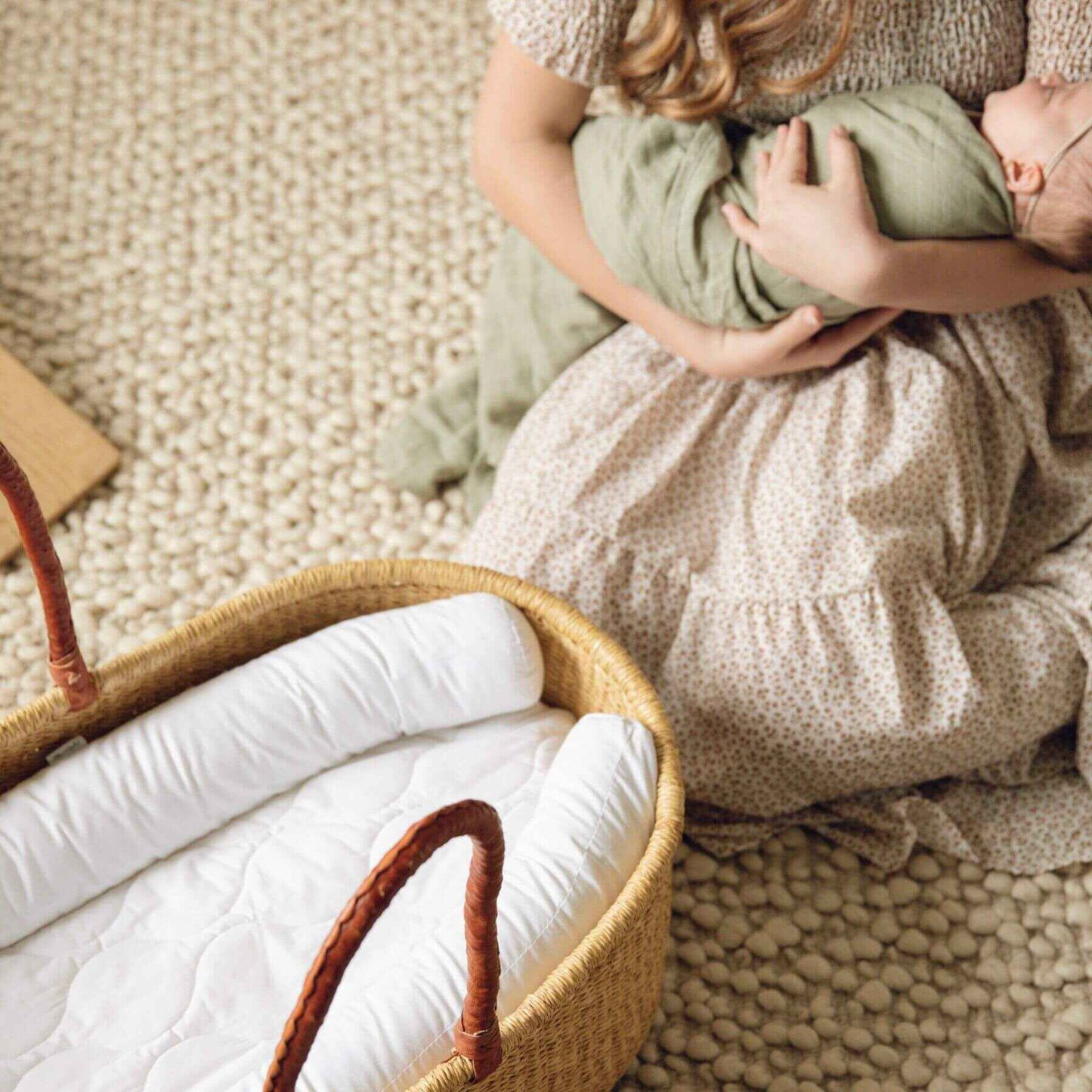 Child holding a baby wrapped in a green blanket next to Plum+Sparrow Nest Lounger on a textured floor.