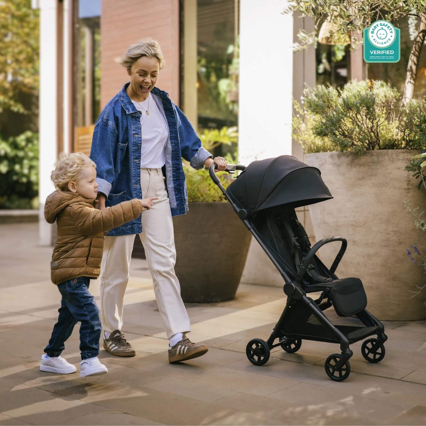 Woman pushing Mompush Nexis Stroller with a child next to her on a sidewalk.