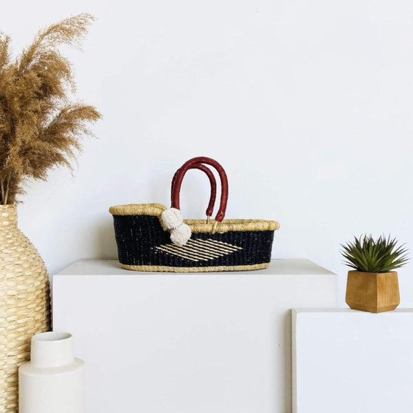 Plum+Sparrow Nightfall Mini Moses Basket on a white surface with decorative items.