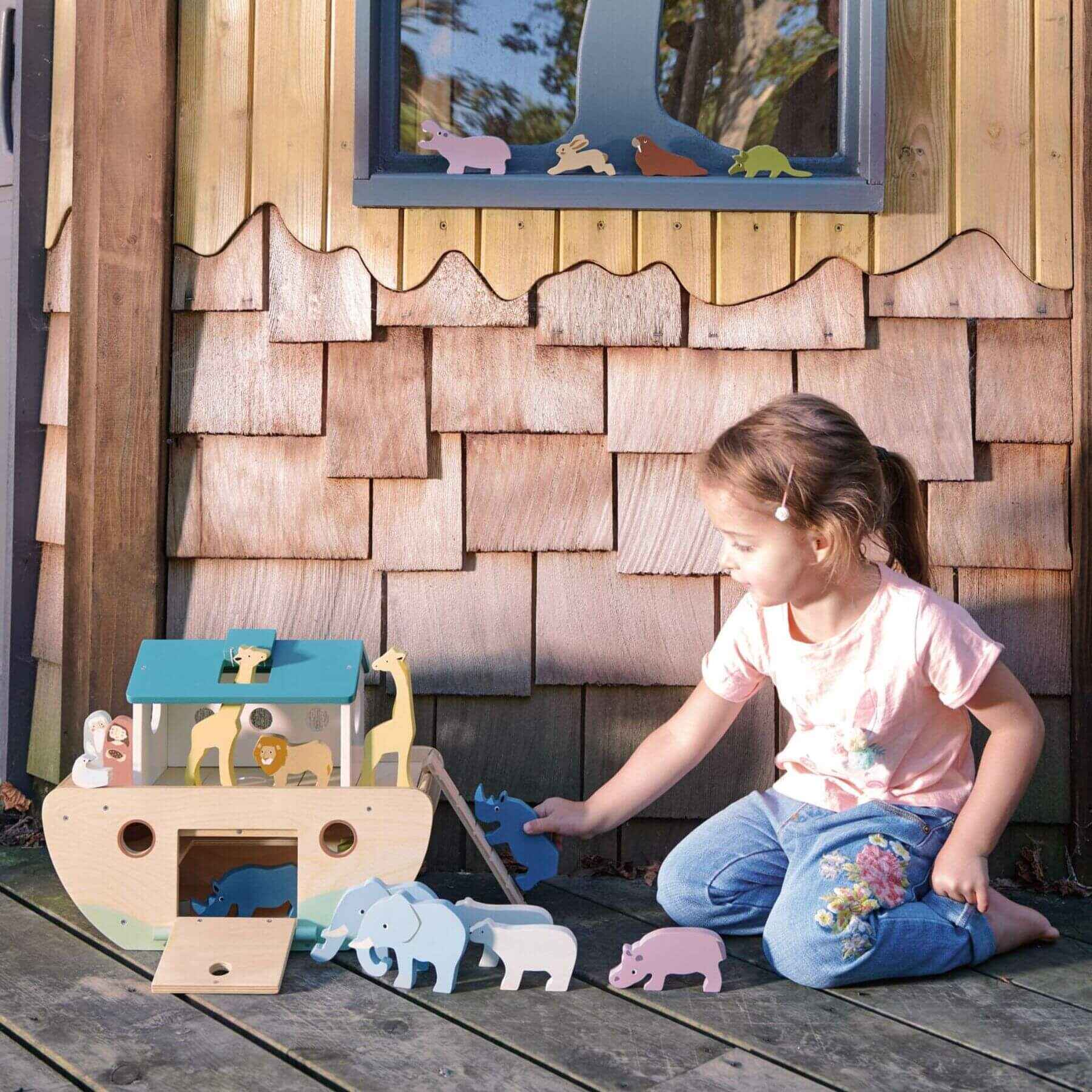 Child playing with Tender Leaf Noah’s Wooden Ark in front of a wooden playhouse.